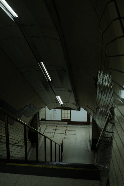 An outdoor railway station platform at Turnham Green, with multiple tracks curving to the right under a concrete and metal overpass. The platform has a light-colored tiled wall with a London Undergrou